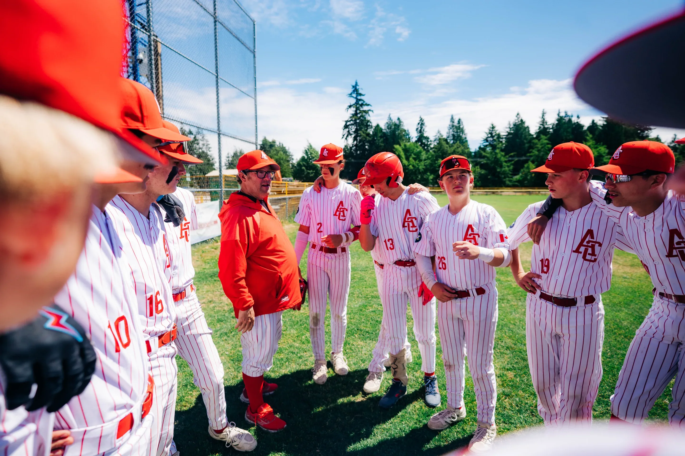 The Cardinals Bantam team in white pinstripes, gathered in a circle around their coach at the Delta game.
