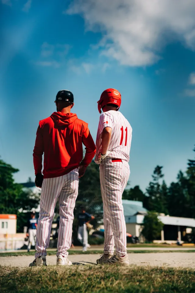 A coach and a player, seen from behind, looking out across the field.