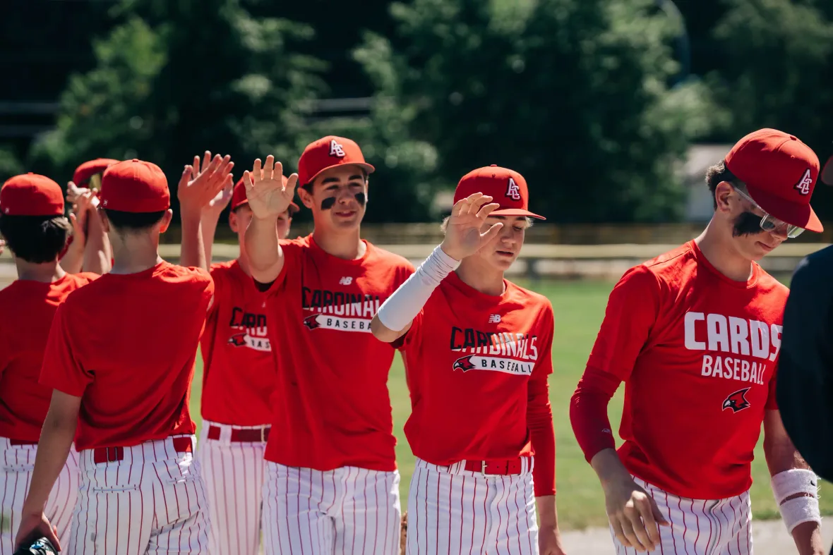 Cardinals players in red club shirts and pinstripe pants high-five their way down the line after a game.