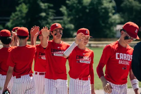 Cardinals players in red club shirts and pinstripe pants high-five their way down the line after a game.
