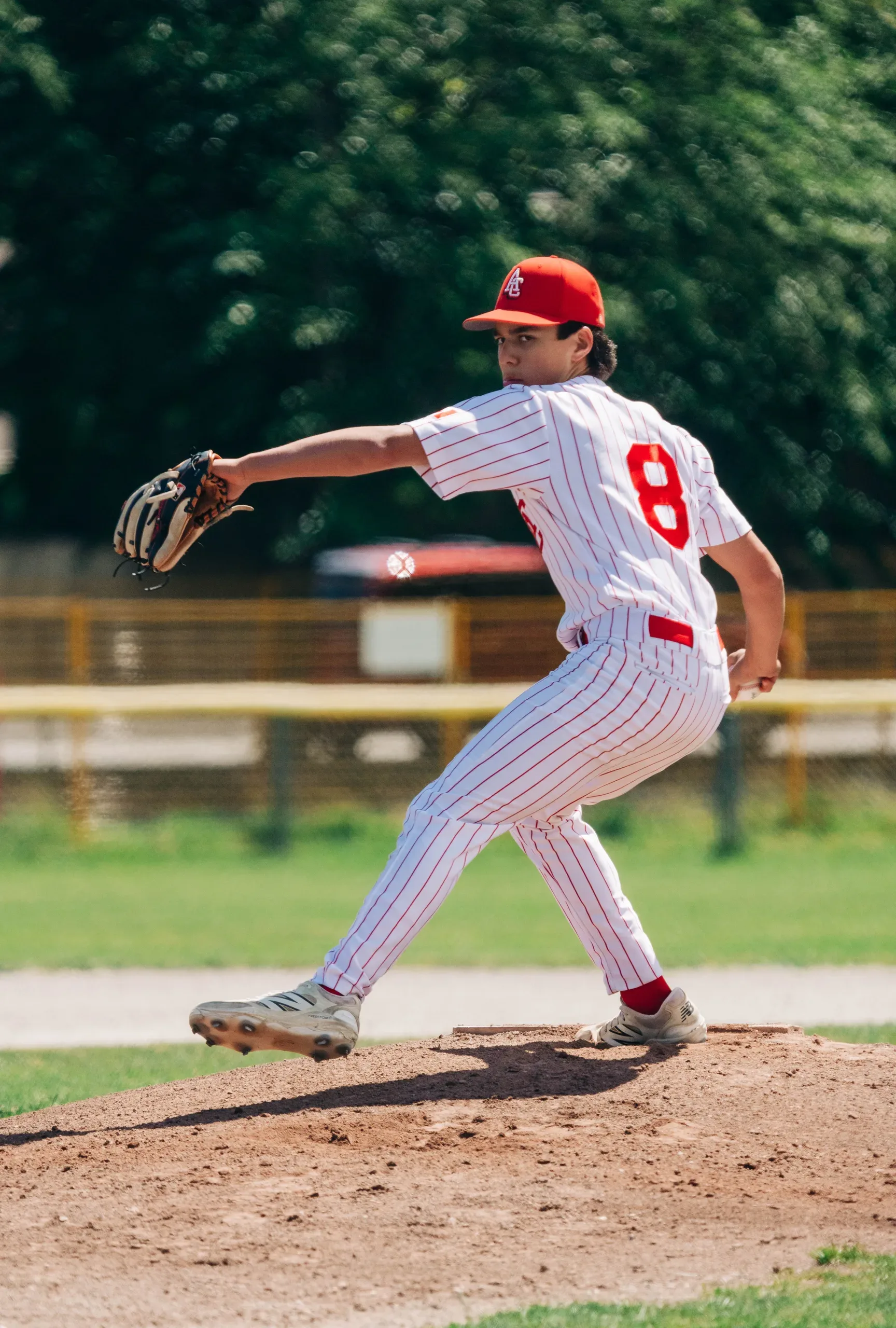 A Cardinals Bantam pitcher in white pinstripes and a red cap, throwing from the mound in a game against Delta.