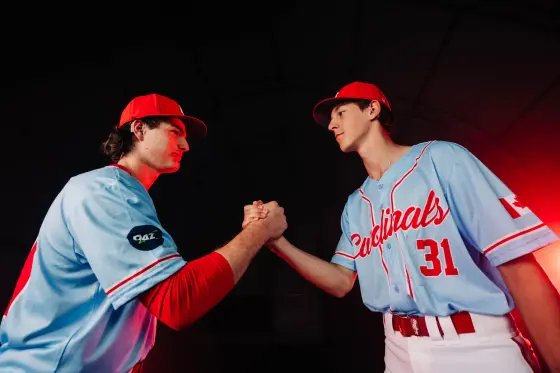 Two Cardinals players clasp hands under the red lights of the training dome.