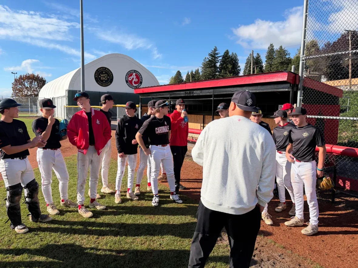 The visitor in the white sweatshirt, seen from behind, talks with a line of Cardinals players in front of the dugout.