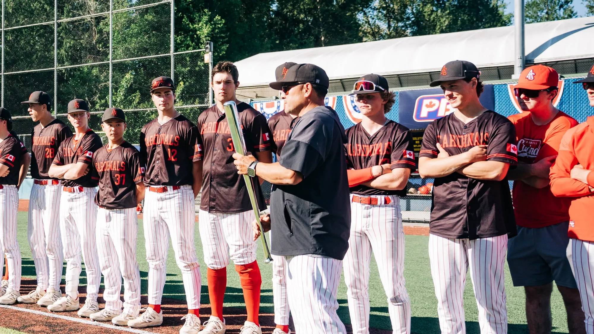 The Cardinals Premier team lined up along the baseline in dark jerseys while a coach in a black shirt talks to them.