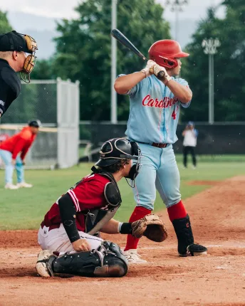 A Cardinals batter set at the plate during a game, with the catcher and umpire in front of him.